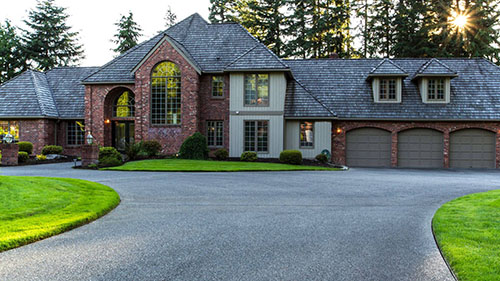 Beautiful brick home with a large curved driveway, surrounded by well-maintained lawn and trees in a residential setting