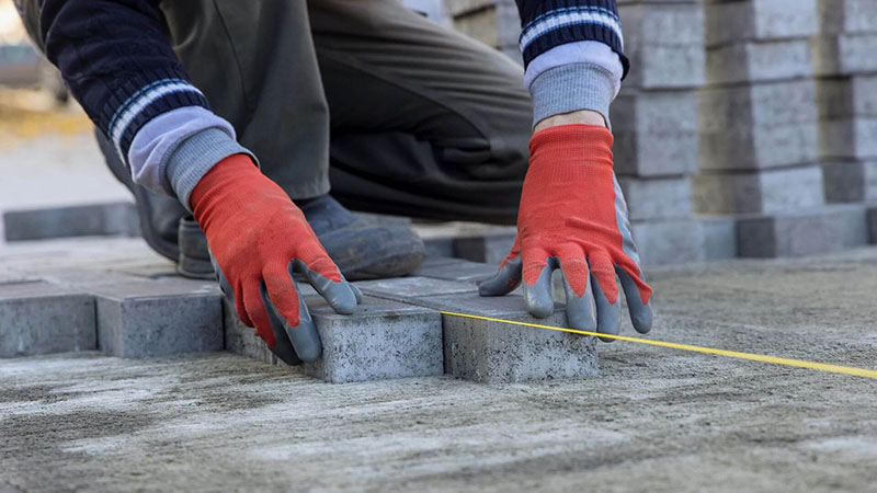 Worker laying concrete pavers with precision, using a measuring line for accurate placement on a prepared surface