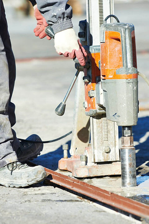 Worker using a drilling machine on a construction site, wearing gloves and safety gear for precision