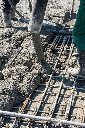 Workers pouring concrete over rebar during construction, with shovels and equipment visible.